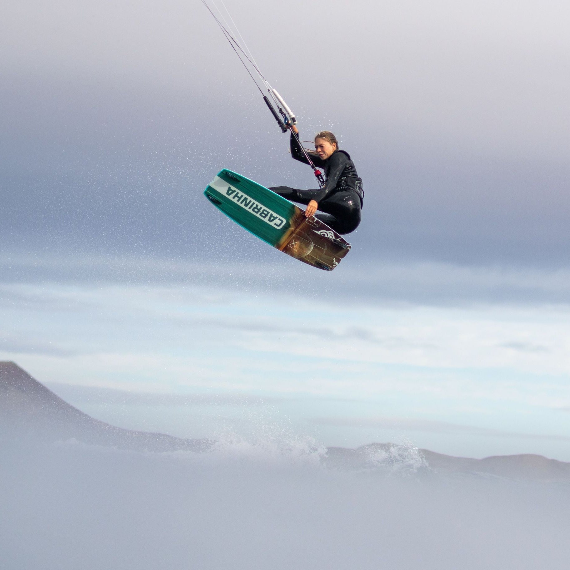Person kiteboarding with a green and white board against a cloudy sky